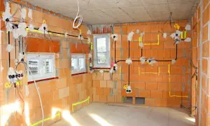 Instalacja elektryczna w nowym budynku. Widoczne przewody, puszki i oznaczenia na ścianach z cegły.