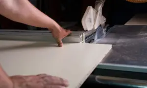 Precyzyjne cięcie płyty meblowej piłą stołową. Ręce prowadzą materiał, pokazując, jak wyciąć otwór w płycie meblowej.