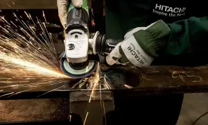 Ręce w rękawicach Hitachi wykonują polerowanie szlifierką kątową, sypią się iskry.