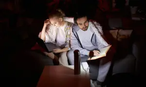 Para radzi sobie z brakiem prądu w części domu, ona pracuje na laptopie, on czyta książkę, oboje okryci kocem.