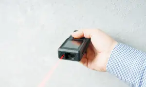 Dłoń trzyma dalmierz laserowy, z którego wychodzi czerwona wiązka. To najlepszy laser do precyzyjnych pomiarów.