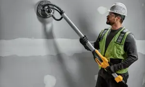Budowlaniec szlifuje ścianę za pomocą szlifierki do gipsu DeWalt.