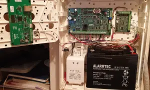 Wnętrze obudowy systemu alarmowego satel. Widoczne płyty główne, akumulator i okablowanie.