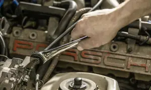 Ręka mechanika używa klucza motylkowego do dokręcania śruby w silniku Porsche.