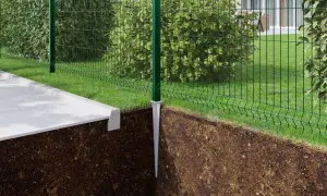 Montaż słupków ogrodzeniowych bez betonu. Metalowy szpic wbity w ziemię, na nim zielony słupek i siatka ogrodzeniowa.