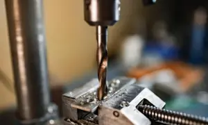 Wiertło wkręca się w metal, tworząc otwór pod gwint. Wióry metalu sypią się wokół.