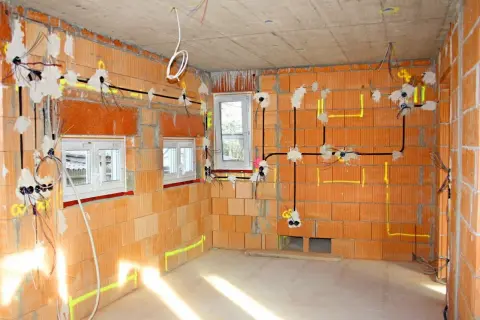 Instalacja elektryczna w nowym budynku. Widoczne przewody, puszki i oznaczenia na ścianach z cegły.