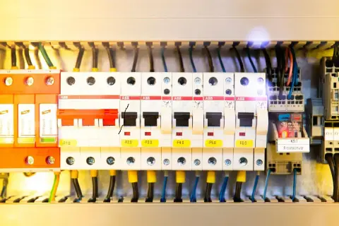 Wnętrze rozdzielni elektrycznej z widocznymi zabezpieczeniami, przewodami i elementami sterującymi.