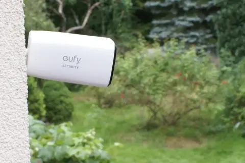 Kamera Eufy Security zapewnia monitoring działki przez internet mobilny. Widok ogrodu z kamerą zamontowaną na ścianie.