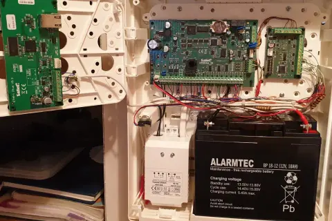 Wnętrze obudowy systemu alarmowego satel. Widoczne płyty główne, akumulator i okablowanie.