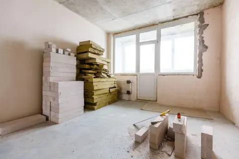 Materiały do ocieplania ścian od wewnątrz styropianem: białe bloczki, żółta wełna mineralna, narzędzia budowlane.