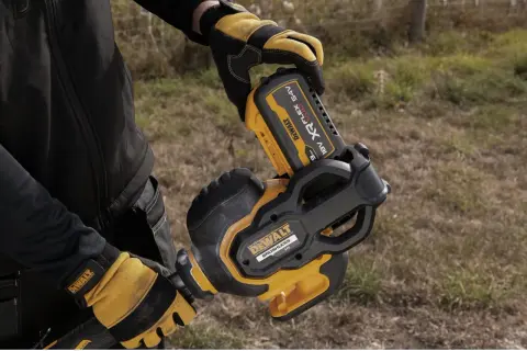 Ręce w rękawicach DeWalt montują akumulator 54V do narzędzia. DeWalt to znana firma produkująca elektronarzędzia.