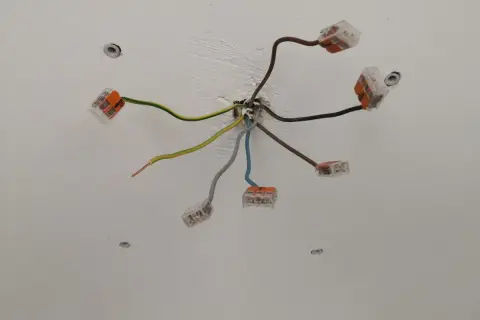 Sufit z instalacją elektryczną. Widać kilka przewodów, w tym czarny kabel elektryczny, połączonych złączkami.