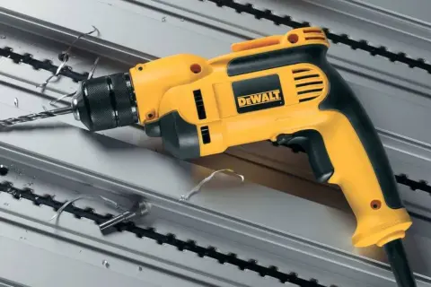 Żółto-czarna wiertarka dwubiegowa bez udaru DeWalt wierci w metalowym profilu, pozostawiając wióry.