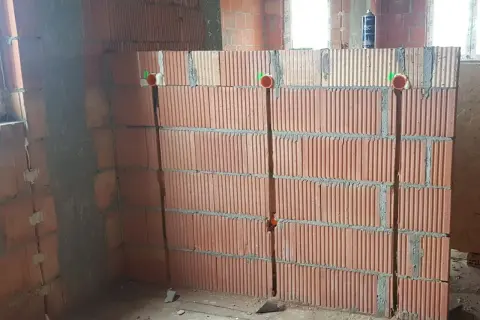 Przygotowanie ścian do instalacji elektrycznej: widoczne bruzdowanie pod kable w ceglanej ścianie, z widocznymi puszkami instalacyjnymi.