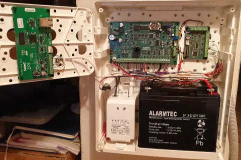 Wnętrze centrali alarmowej Satel z modułem ETHM-1 Plus, płytą główną Integra i akumulatorem.