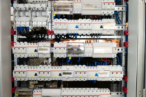 Panel elektryczny z licznymi wyłącznikami i zabezpieczeniami, połączonymi przewodami. Widać tu szyny elektryczne, które stanowią podstawę montażu.