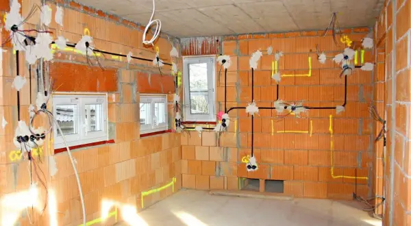 Instalacja elektryczna w nowym budynku. Widoczne przewody, puszki i oznaczenia na ścianach z cegły.