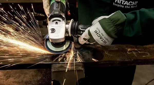 Ręce w rękawicach Hitachi wykonują polerowanie szlifierką kątową, sypią się iskry.