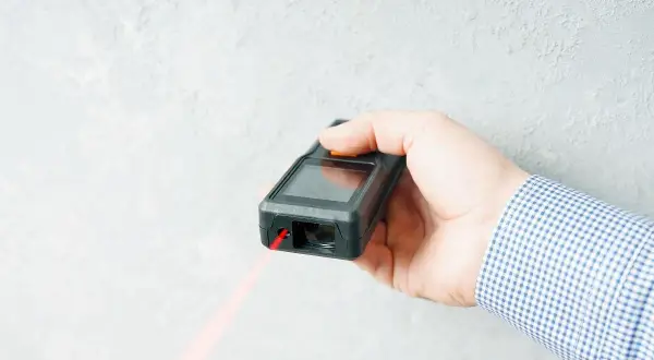 Dłoń trzyma dalmierz laserowy, z którego wychodzi czerwona wiązka. To najlepszy laser do precyzyjnych pomiarów.