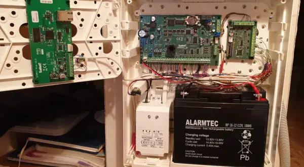 Wnętrze obudowy systemu alarmowego satel. Widoczne płyty główne, akumulator i okablowanie.