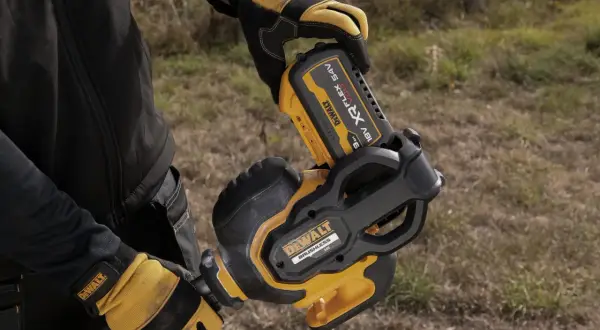 Ręce w rękawicach DeWalt montują akumulator 54V do narzędzia. DeWalt to znana firma produkująca elektronarzędzia.