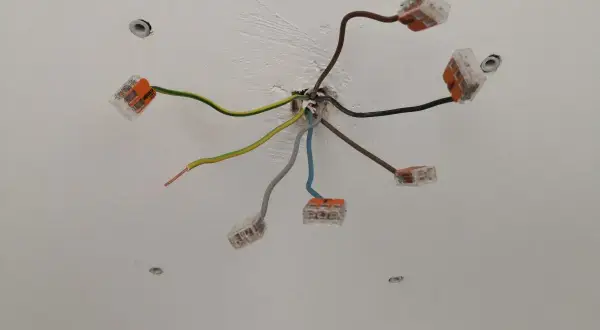 Sufit z instalacją elektryczną. Widać kilka przewodów, w tym czarny kabel elektryczny, połączonych złączkami.