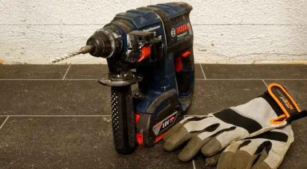 Mocna wiertarka udarowa Bosch z zamontowanym wiertłem i rękawicami roboczymi obok. Dowiedz się, jak wyjąć wiertło z wiertarki.