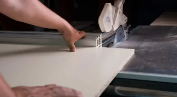 Precyzyjne cięcie płyty MDF na pile stołowej. Ręce stolarza prowadzą materiał do obracającego się ostrza.