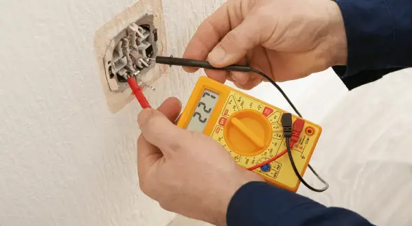 Elektryk mierzy napięcie w gniazdku. Wynik 227V sugeruje, że słaby prąd w domu to nie problem, a prawidłowe działanie instalacji.