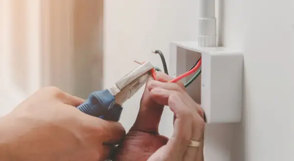 Elektryk podłącza przewody, używając szczypiec. Widoczne oznaczenie prądu L na czerwonym kablu.
