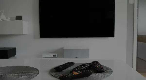 Na stole leży kilka pilotów, gotowych do obsługi czarnego ekranu telewizora wiszącego na ścianie.