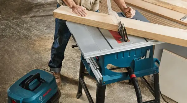 Stolarz precyzyjnie tnie drewno na pile stołowej Bosch GTS 254. Obok stoi odkurzacz warsztatowy Bosch.