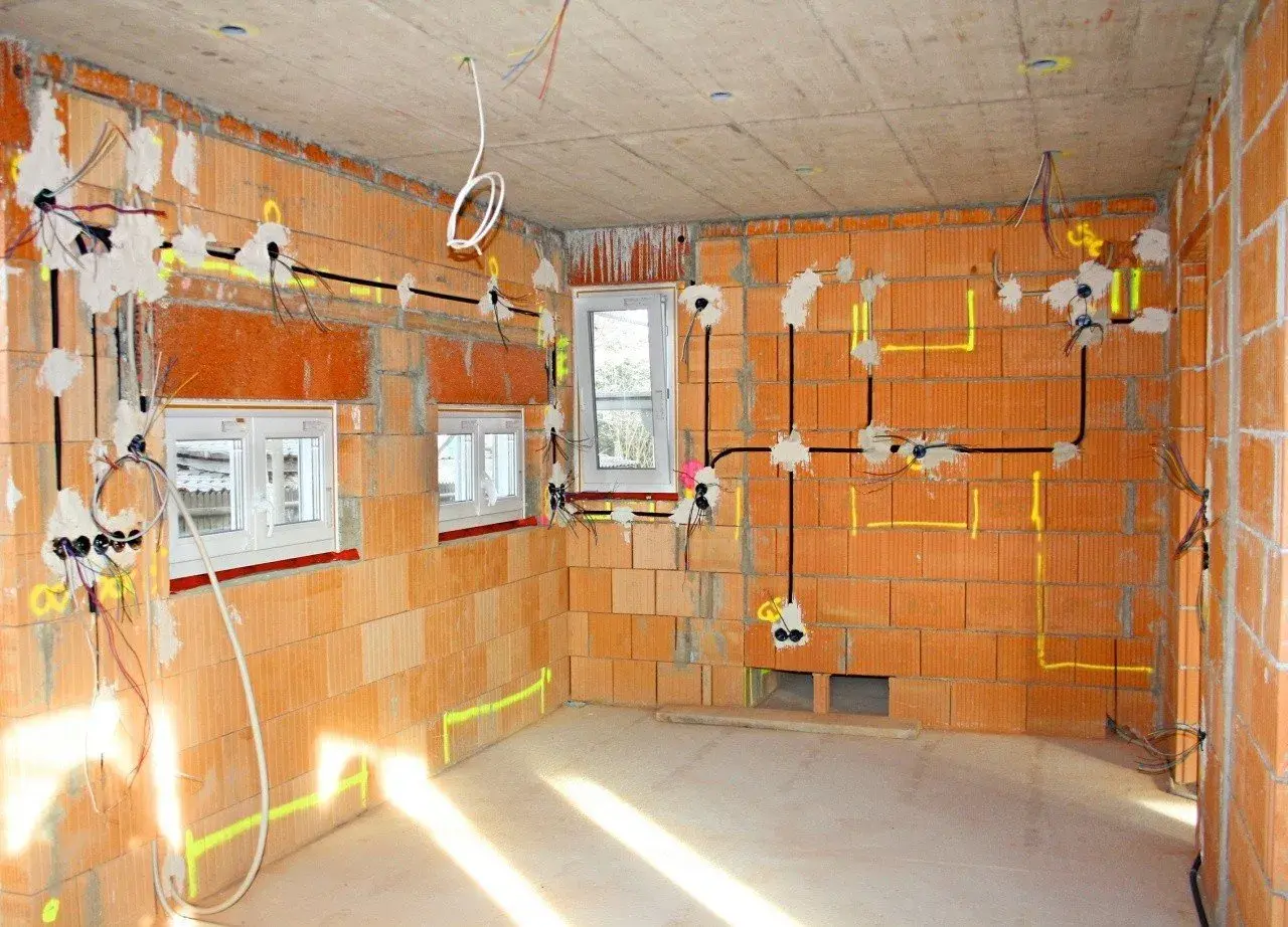 Instalacja elektryczna w nowym budynku. Widoczne przewody, puszki i oznaczenia na ścianach z cegły.