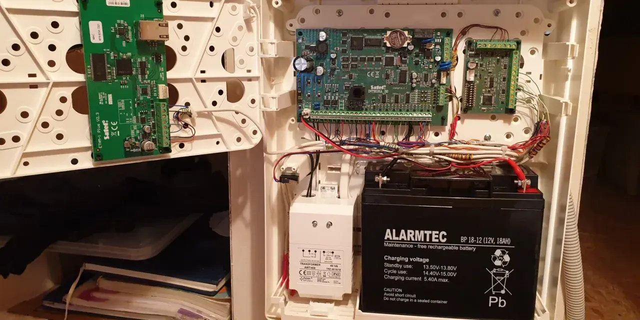 Wnętrze obudowy systemu alarmowego satel. Widoczne płyty główne, akumulator i okablowanie.