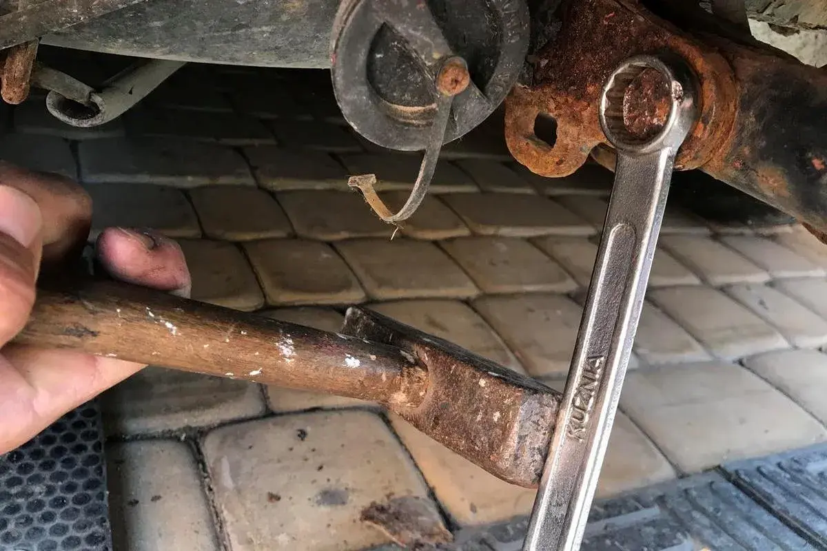 Próba odkręcenia zapieczonej śruby kluczem i młotkiem. Ręka trzyma młotek, klucz nasadowy na śrubie.