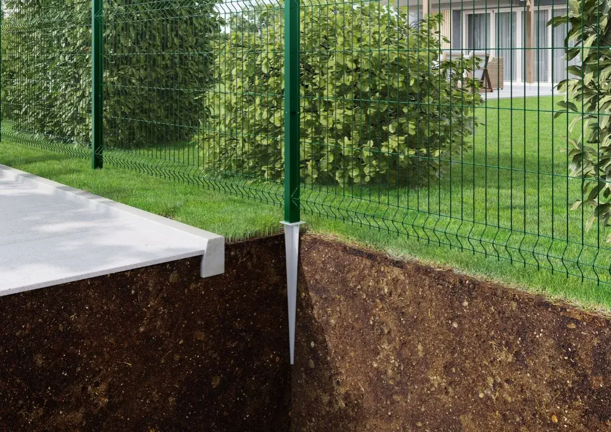 Montaż słupków ogrodzeniowych bez betonu. Metalowy szpic wbity w ziemię, na nim zielony słupek i siatka ogrodzeniowa.