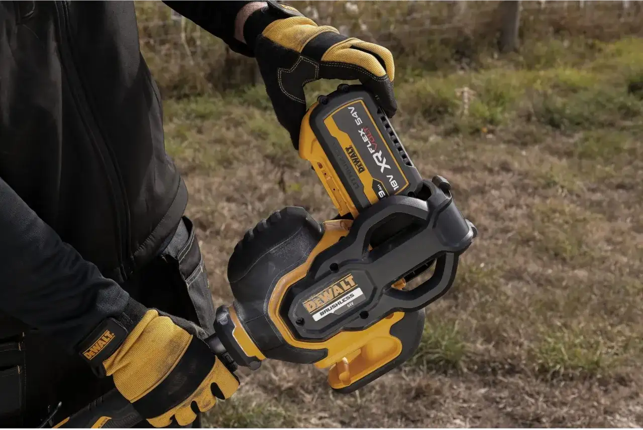 Ręce w rękawicach DeWalt montują akumulator 54V do narzędzia. DeWalt to znana firma produkująca elektronarzędzia.