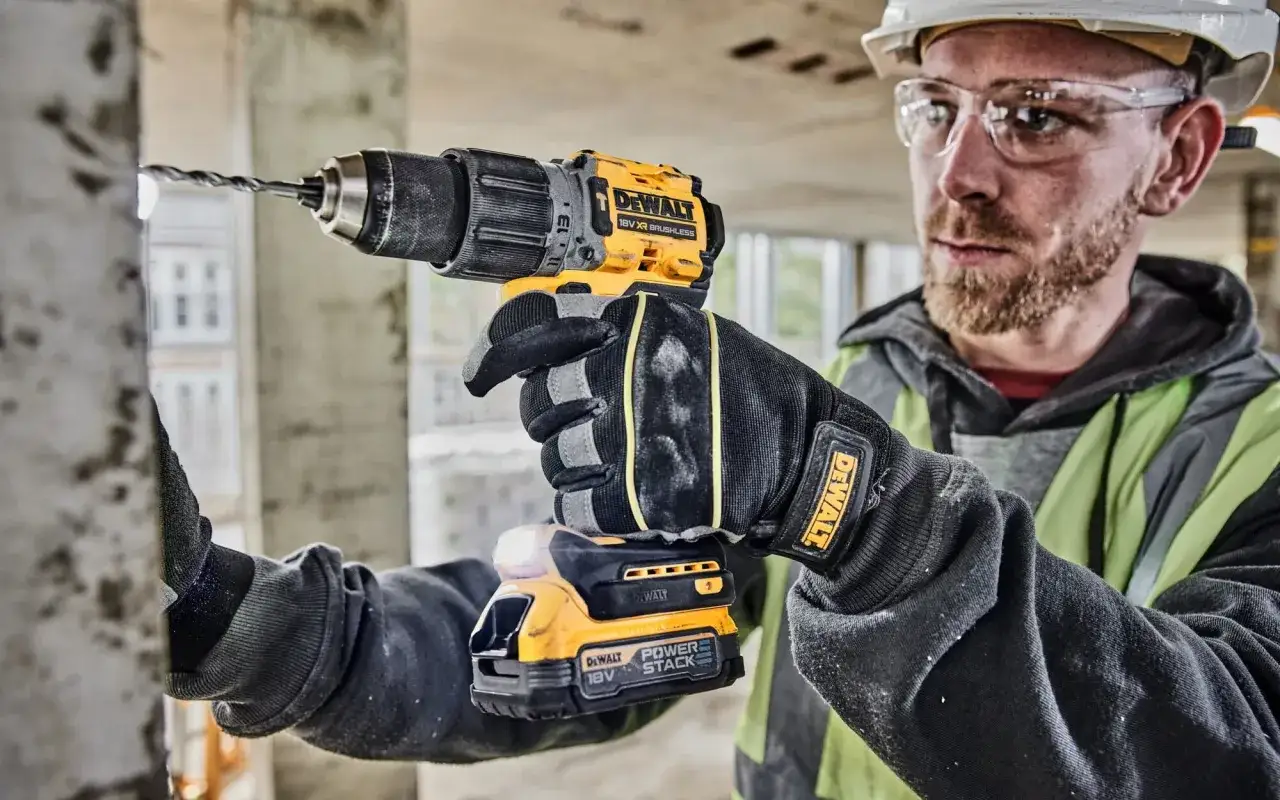Budowlaniec w rękawicach z logo DeWalt wierci w betonie. DeWalt to znana marka narzędzi budowlanych.