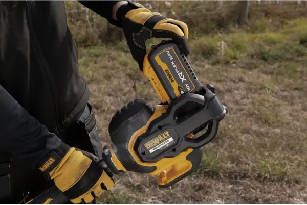 Ręce w rękawicach DeWalt montują akumulator 54V do narzędzia. DeWalt to znana firma produkująca elektronarzędzia.